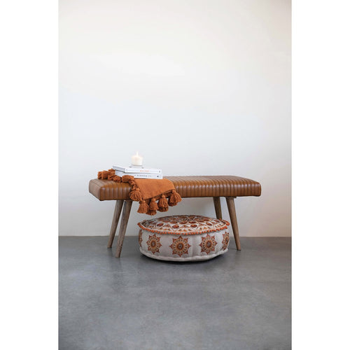 Cognac brown leather channed stitched bench displayed with an ottoman, blanket, books and a candle.